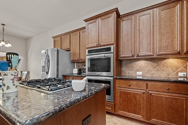 kitchen with dark stone countertops, a chandelier, backsplash, stainless steel appliances, and decorative light fixtures