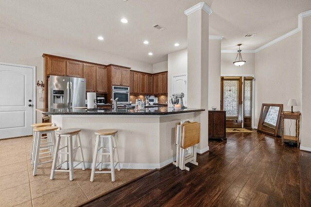 kitchen with kitchen peninsula, hanging light fixtures, ornamental molding, a breakfast bar, and stainless steel appliances