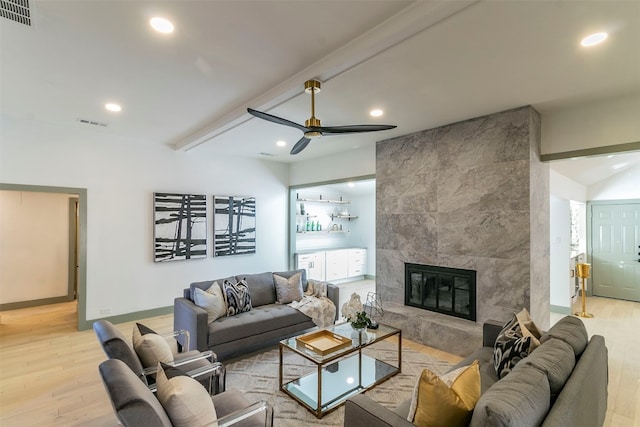 living room featuring a fireplace, beam ceiling, ceiling fan, light hardwood / wood-style flooring, and tile walls