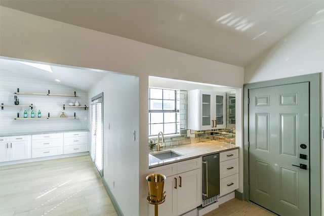 kitchen with vaulted ceiling with skylight, white cabinetry, sink, and tasteful backsplash