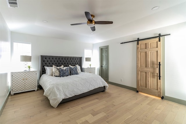 bedroom featuring a barn door, ceiling fan, and light hardwood / wood-style flooring