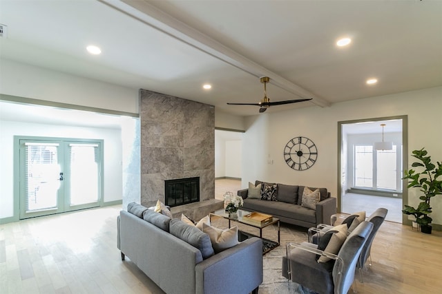 living room with a tile fireplace, beamed ceiling, french doors, light hardwood / wood-style flooring, and ceiling fan