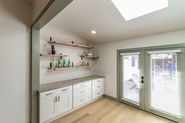 bar featuring vaulted ceiling, french doors, light hardwood / wood-style flooring, white cabinets, and backsplash