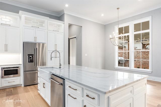 kitchen with an island with sink, hanging light fixtures, appliances with stainless steel finishes, and light hardwood / wood-style flooring