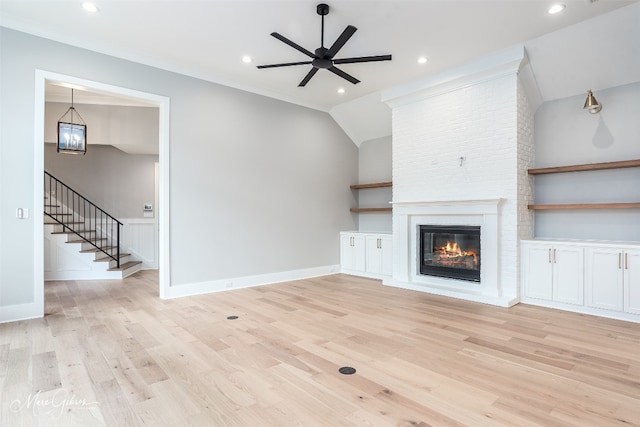 unfurnished living room featuring light hardwood / wood-style flooring, ceiling fan with notable chandelier, and a large fireplace