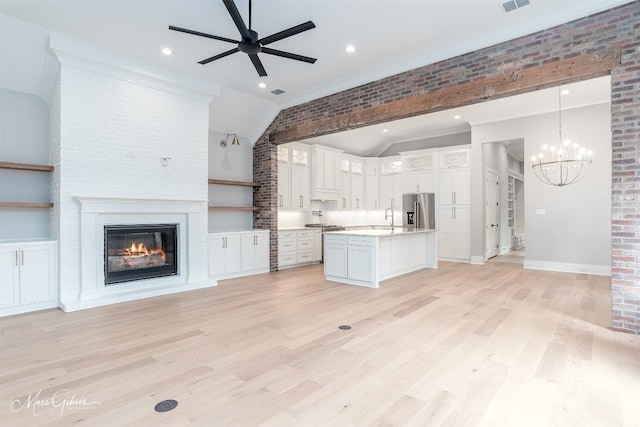 unfurnished living room with a fireplace, brick wall, ceiling fan with notable chandelier, and light wood-type flooring