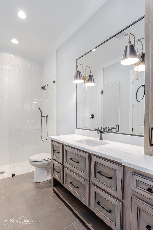 bathroom featuring toilet, tile flooring, a tile shower, and vanity