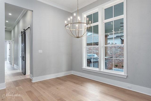 unfurnished dining area with crown molding, a notable chandelier, light wood-type flooring, and a barn door