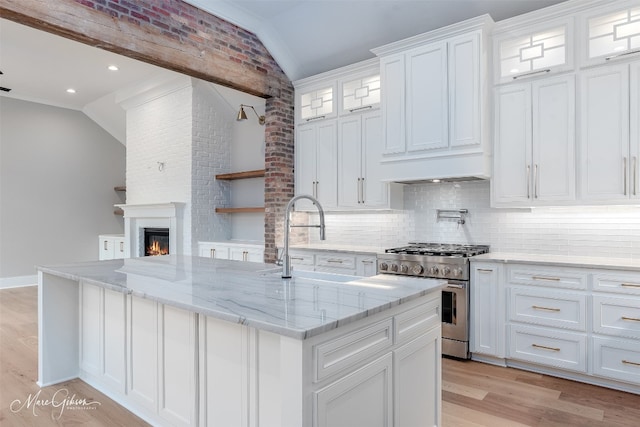 kitchen with tasteful backsplash, stainless steel stove, vaulted ceiling, light hardwood / wood-style floors, and white cabinets