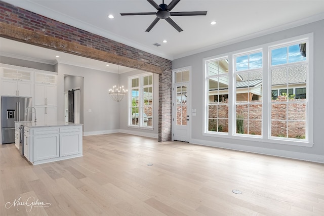 unfurnished living room with ceiling fan with notable chandelier, brick wall, a barn door, light hardwood / wood-style flooring, and ornamental molding