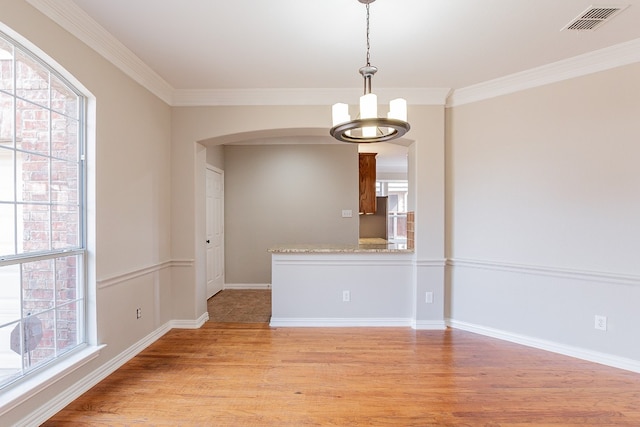 unfurnished room with a wealth of natural light, ornamental molding, light wood-type flooring, and an inviting chandelier