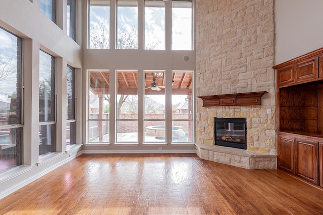 unfurnished living room with a high ceiling, light hardwood / wood-style floors, a stone fireplace, and a wealth of natural light