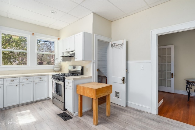 kitchen with light hardwood / wood-style floors, stainless steel range with gas cooktop, white cabinets, and a drop ceiling