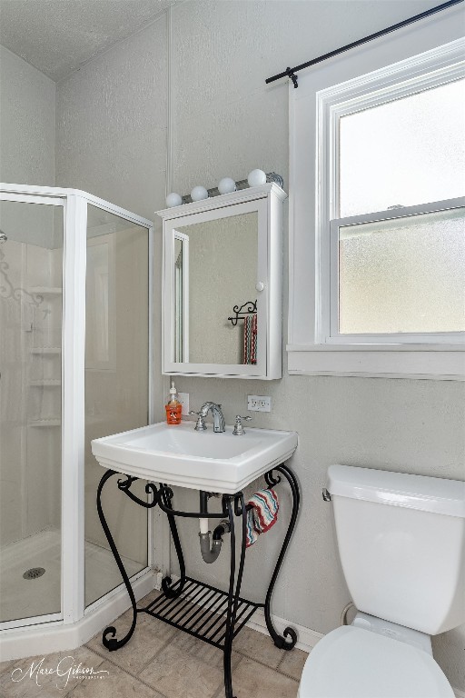 bathroom with toilet, a shower with door, and tile flooring