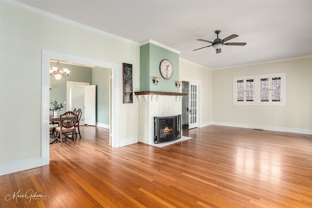 unfurnished living room featuring ornamental molding, hardwood / wood-style floors, ceiling fan with notable chandelier, and a brick fireplace