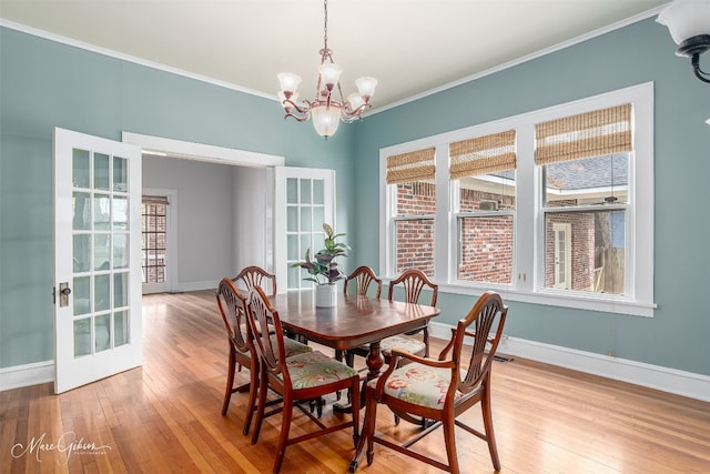 dining area with french doors, ornamental molding, a notable chandelier, and light wood-type flooring