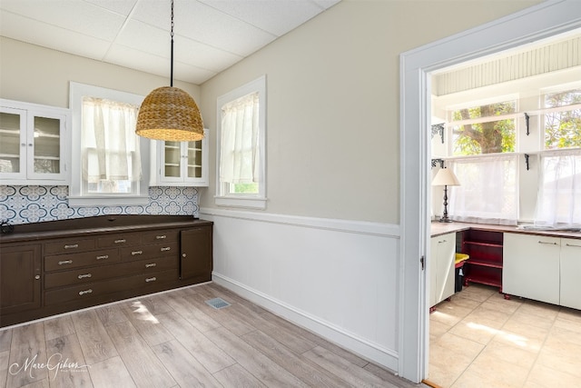 kitchen featuring dark brown cabinetry, backsplash, decorative light fixtures, white cabinetry, and built in desk