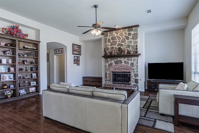 living room with plenty of natural light, ceiling fan, dark wood-type flooring, and a stone fireplace