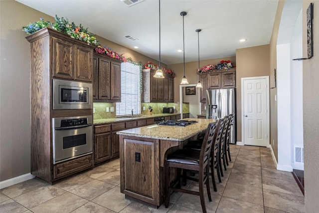 kitchen with light stone counters, tasteful backsplash, dark brown cabinets, stainless steel appliances, and a center island