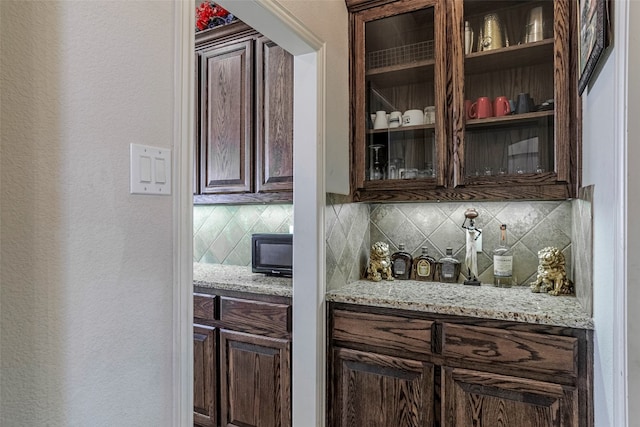 bar featuring light stone countertops, dark brown cabinets, and tasteful backsplash