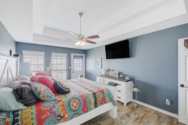 bedroom with wood-type flooring, ceiling fan, and a tray ceiling