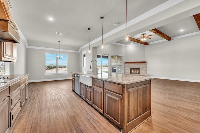 kitchen featuring a spacious island, a stone fireplace, pendant lighting, sink, and light hardwood / wood-style flooring