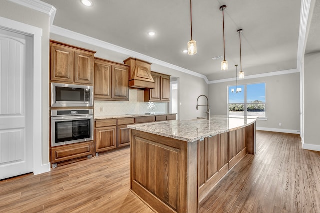 kitchen with hanging light fixtures, an island with sink, light wood-type flooring, appliances with stainless steel finishes, and premium range hood