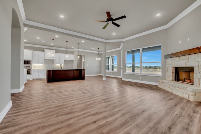 unfurnished living room with a stone fireplace, sink, light hardwood / wood-style flooring, and ornamental molding