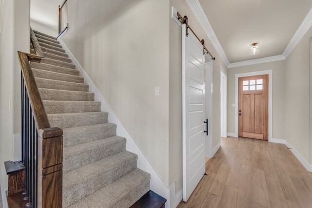 foyer with a barn door, light hardwood / wood-style floors, and ornamental molding