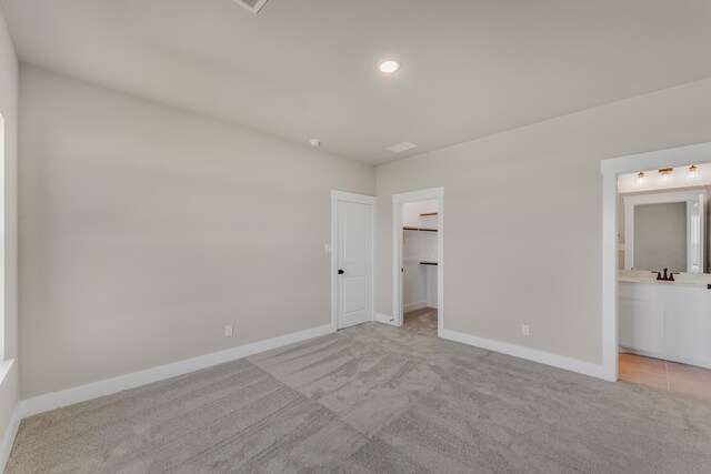 unfurnished bedroom featuring a spacious closet, ensuite bath, light carpet, and a closet