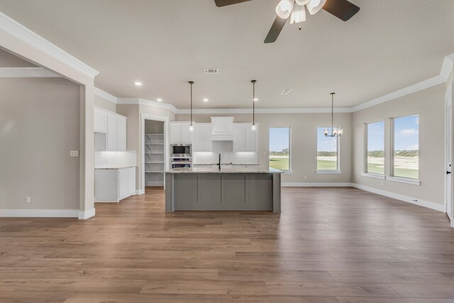 kitchen with light wood-type flooring, white cabinetry, a spacious island, ceiling fan with notable chandelier, and crown molding