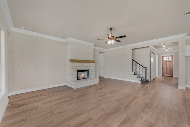 unfurnished living room featuring light wood-type flooring, crown molding, a stone fireplace, and ceiling fan