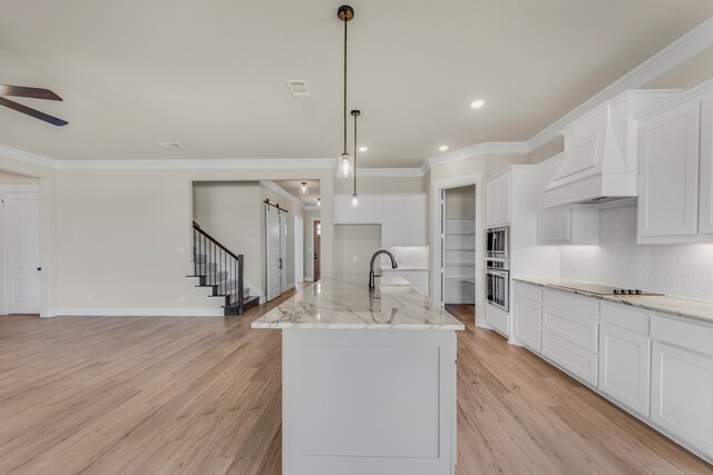 kitchen with light wood-type flooring, ceiling fan, pendant lighting, and an island with sink