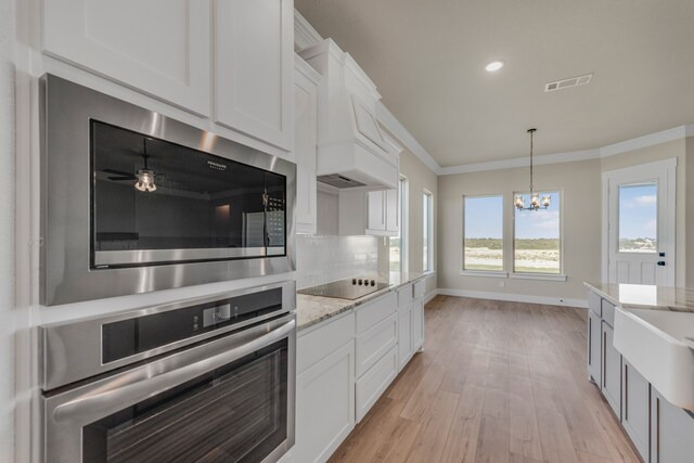 kitchen featuring custom exhaust hood, white cabinetry, stainless steel appliances, an inviting chandelier, and light wood-type flooring