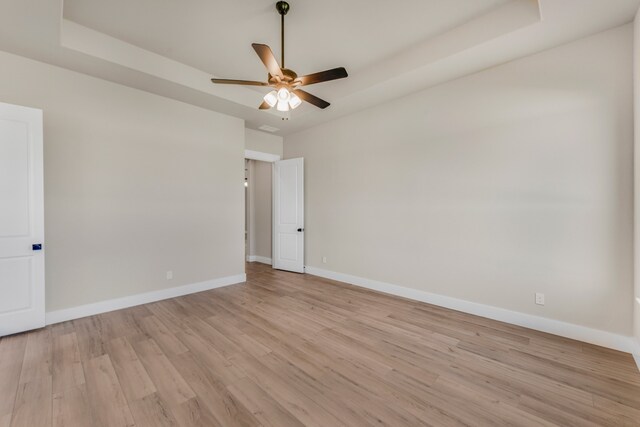 spare room with a tray ceiling, ceiling fan, and light hardwood / wood-style flooring