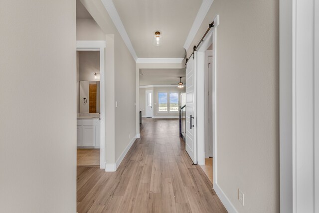 hallway with light hardwood / wood-style flooring, crown molding, and a barn door