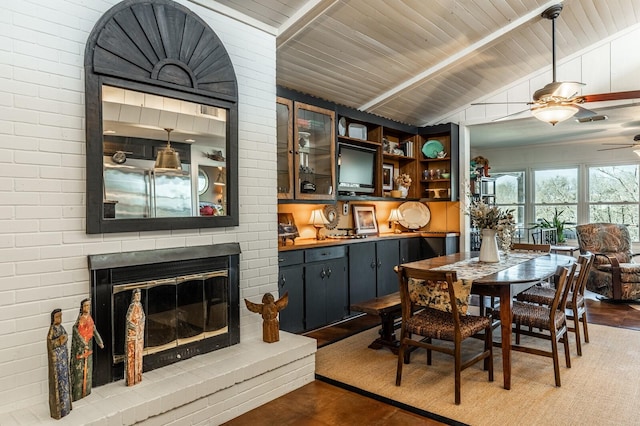 dining room featuring dark wood-style flooring, a fireplace, vaulted ceiling with beams, a ceiling fan, and wood ceiling