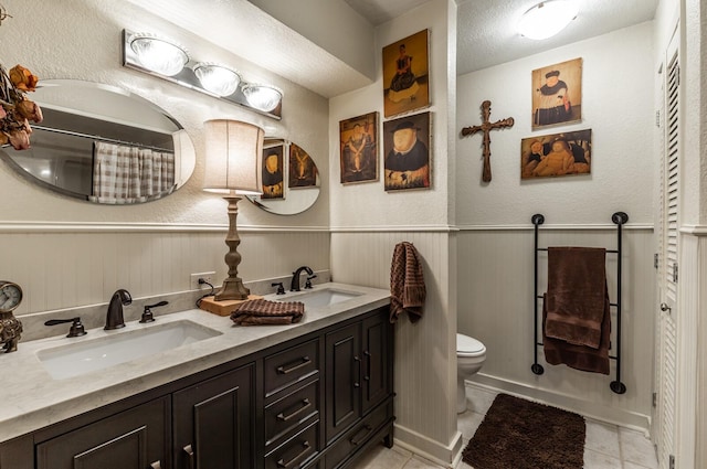 bathroom with toilet, a wainscoted wall, tile patterned flooring, and a sink