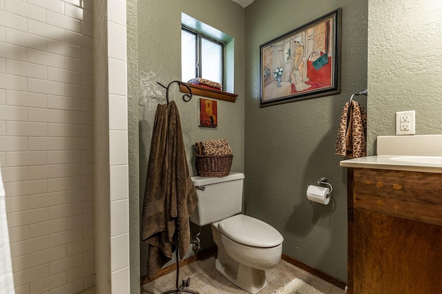 bathroom featuring baseboards, a textured wall, vanity, and toilet