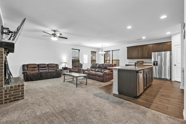 living room with ceiling fan with notable chandelier, dark hardwood / wood-style floors, sink, and a fireplace