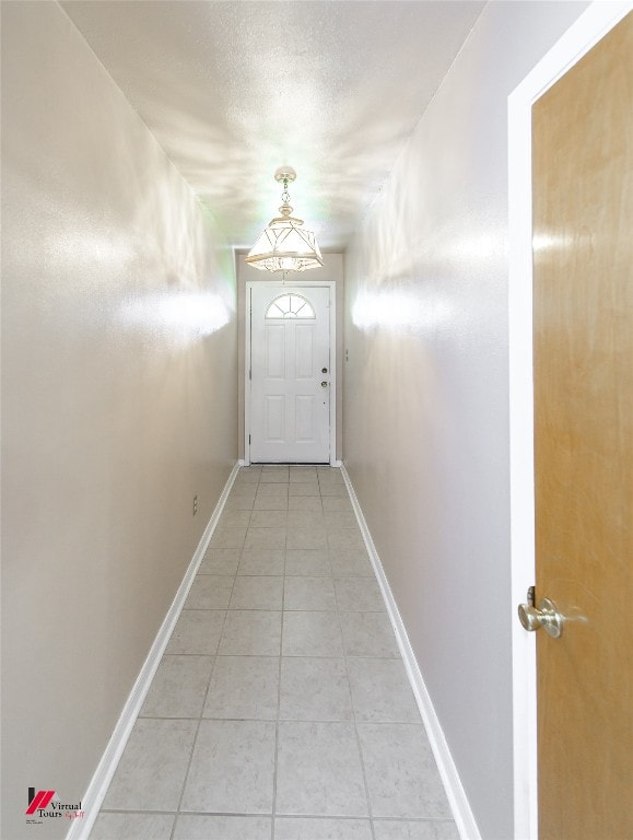 doorway with light tile patterned floors, a textured ceiling, and baseboards