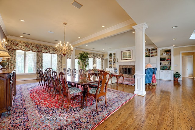 dining room featuring dark hardwood / wood-style floors, built in shelves, crown molding, ornate columns, and an inviting chandelier