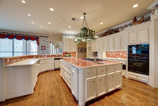 kitchen featuring tasteful backsplash, an island with sink, black double oven, and white cabinetry