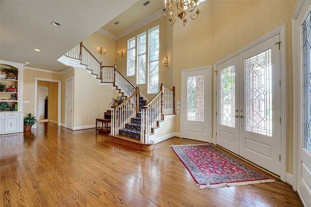 foyer with french doors, an inviting chandelier, ornamental molding, and light wood-type flooring