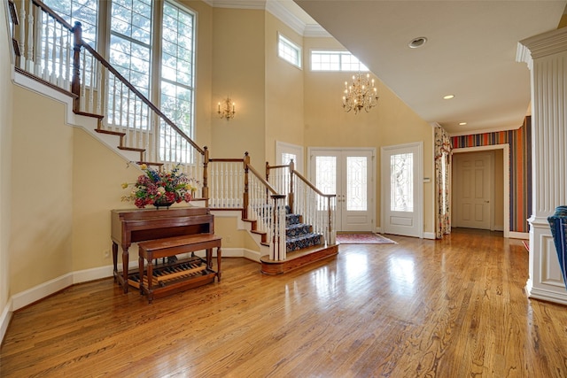 foyer entrance with a towering ceiling, crown molding, light wood-type flooring, and an inviting chandelier