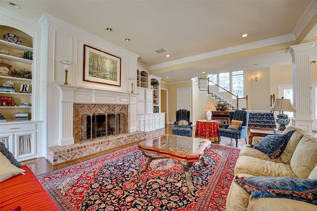 living room featuring crown molding, hardwood / wood-style floors, built in features, a fireplace, and ornate columns