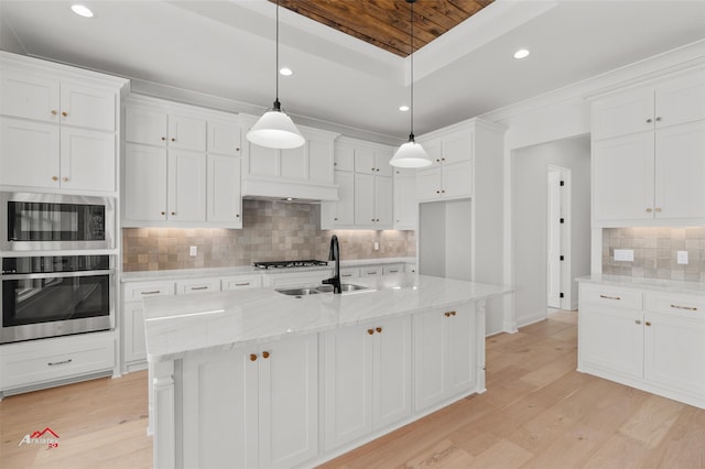 kitchen with light wood-type flooring, light stone counters, backsplash, sink, and white cabinetry