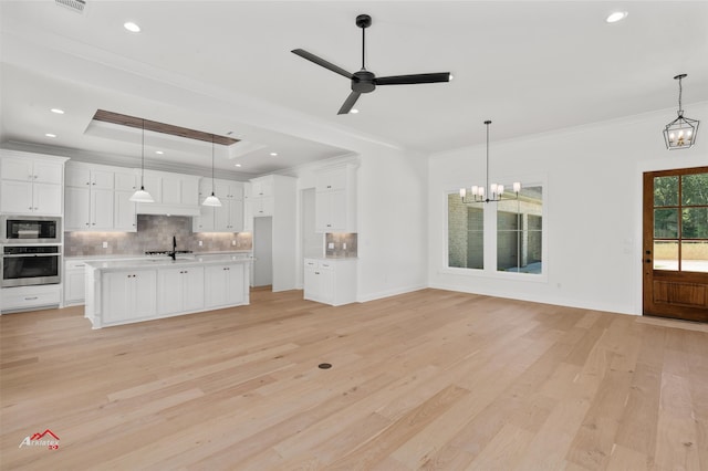 unfurnished living room featuring ornamental molding, a tray ceiling, light wood-type flooring, and ceiling fan with notable chandelier