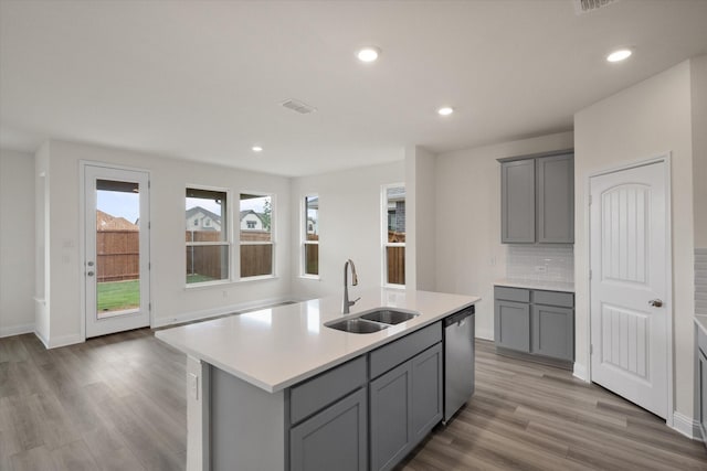 kitchen featuring decorative backsplash, stainless steel dishwasher, a kitchen island with sink, light hardwood / wood-style flooring, and gray cabinets