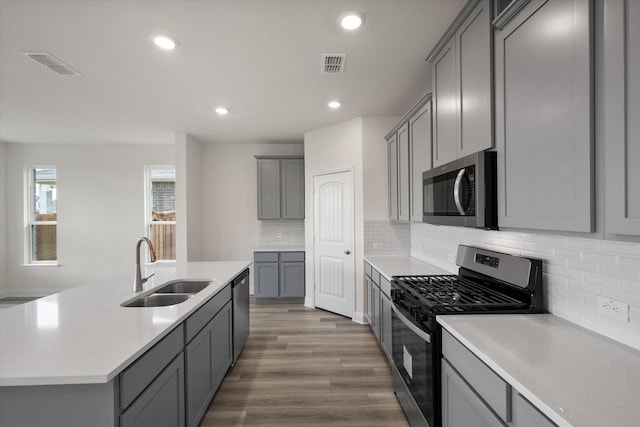 kitchen featuring gray cabinetry, sink, stainless steel appliances, a kitchen island with sink, and hardwood / wood-style flooring